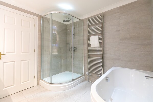 A modern bathroom with a glass-enclosed shower, a white bathtub, and a towel rack.