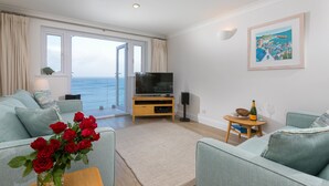 A modern living room with a large window, a flat-screen TV, and a cozy seating area. - Wavetop (St Ives)