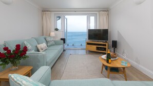 A modern living room with a sofa, TV, and a view of the sea through a large window. - Wavetop (St Ives)
