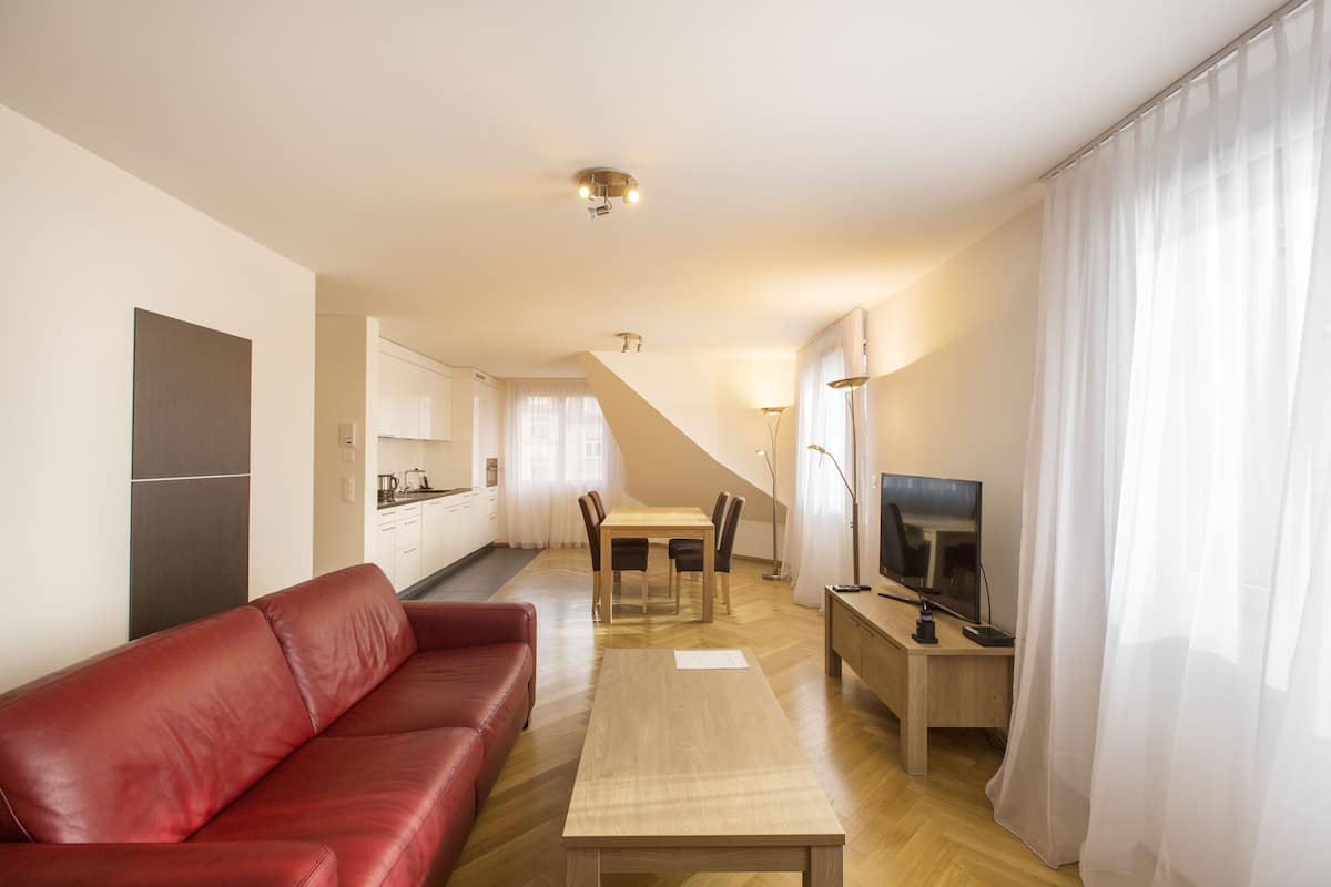 Un appartement moderne avec un canapé en cuir rouge, une table à manger en bois, un téléviseur et une cuisine en arrière-plan.