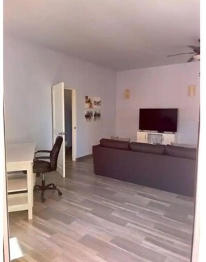 Relax in comfort with a seating area and workspace, featuring a large TV, sofa, and desk.