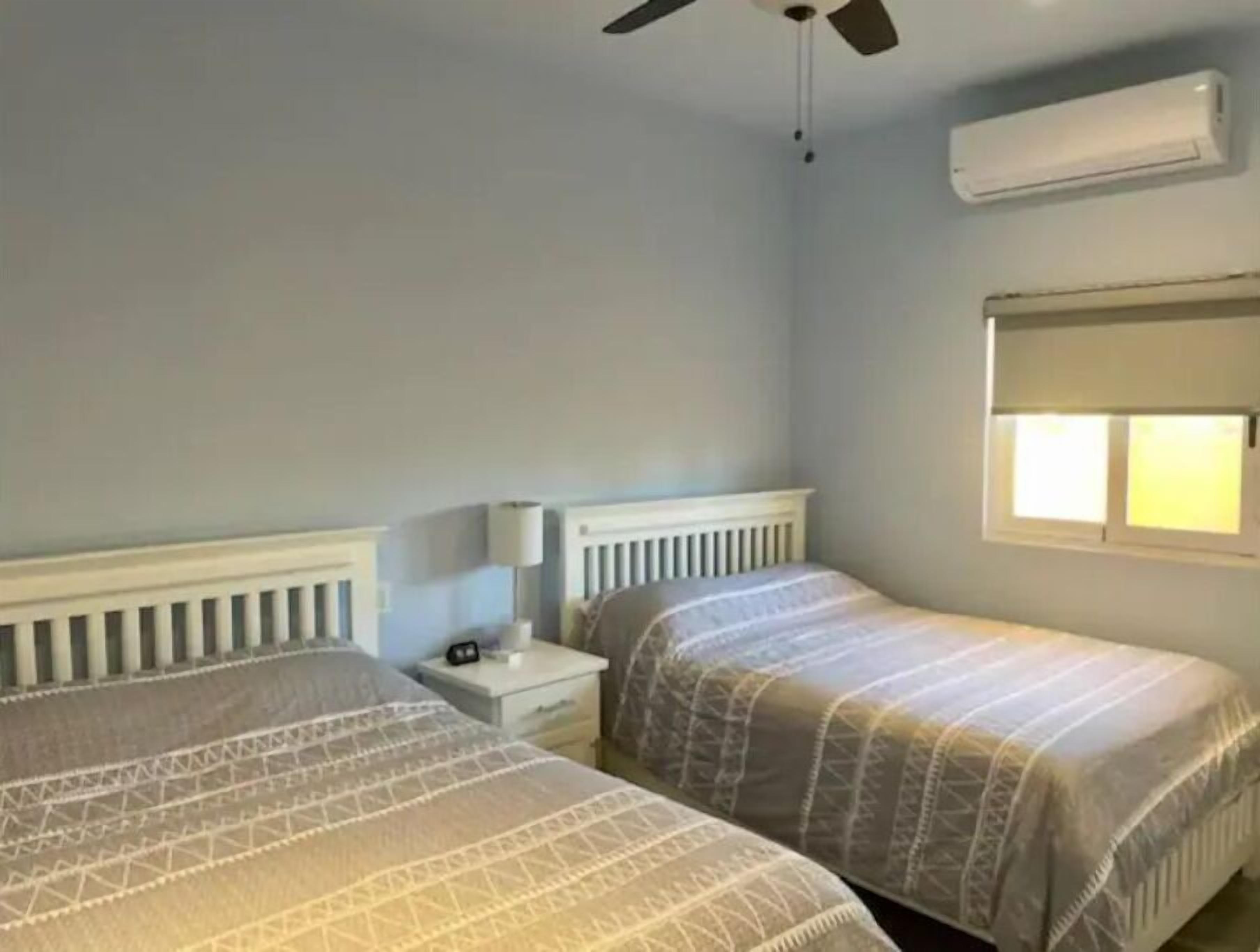A bedroom with two beds, a nightstand, a ceiling fan, and an air conditioning unit.