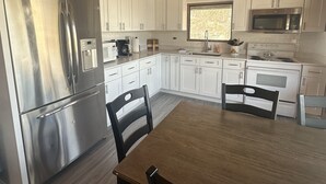A modern kitchen with white cabinets, stainless steel appliances, and a wooden ceiling.
