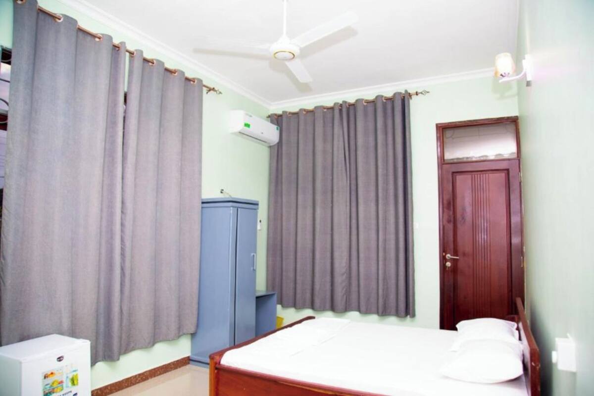 A bedroom with a bed, a ceiling fan, a wardrobe, and a door.