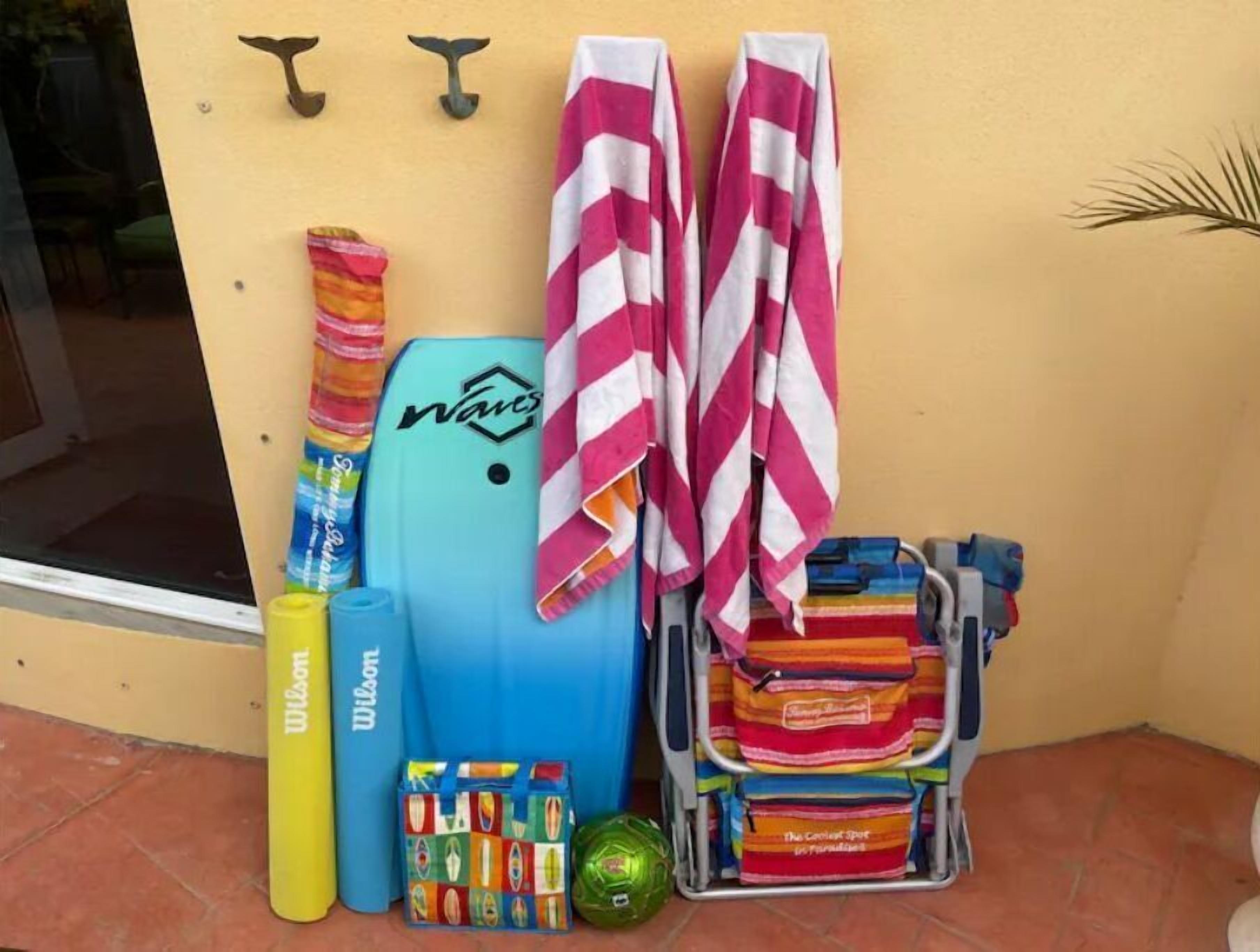 Un espace aménagé au bord de la piscine, avec un flotteur bleu, un flotteur jaune de la marque Wilson, un sac de plage coloré et une pile de serviettes.