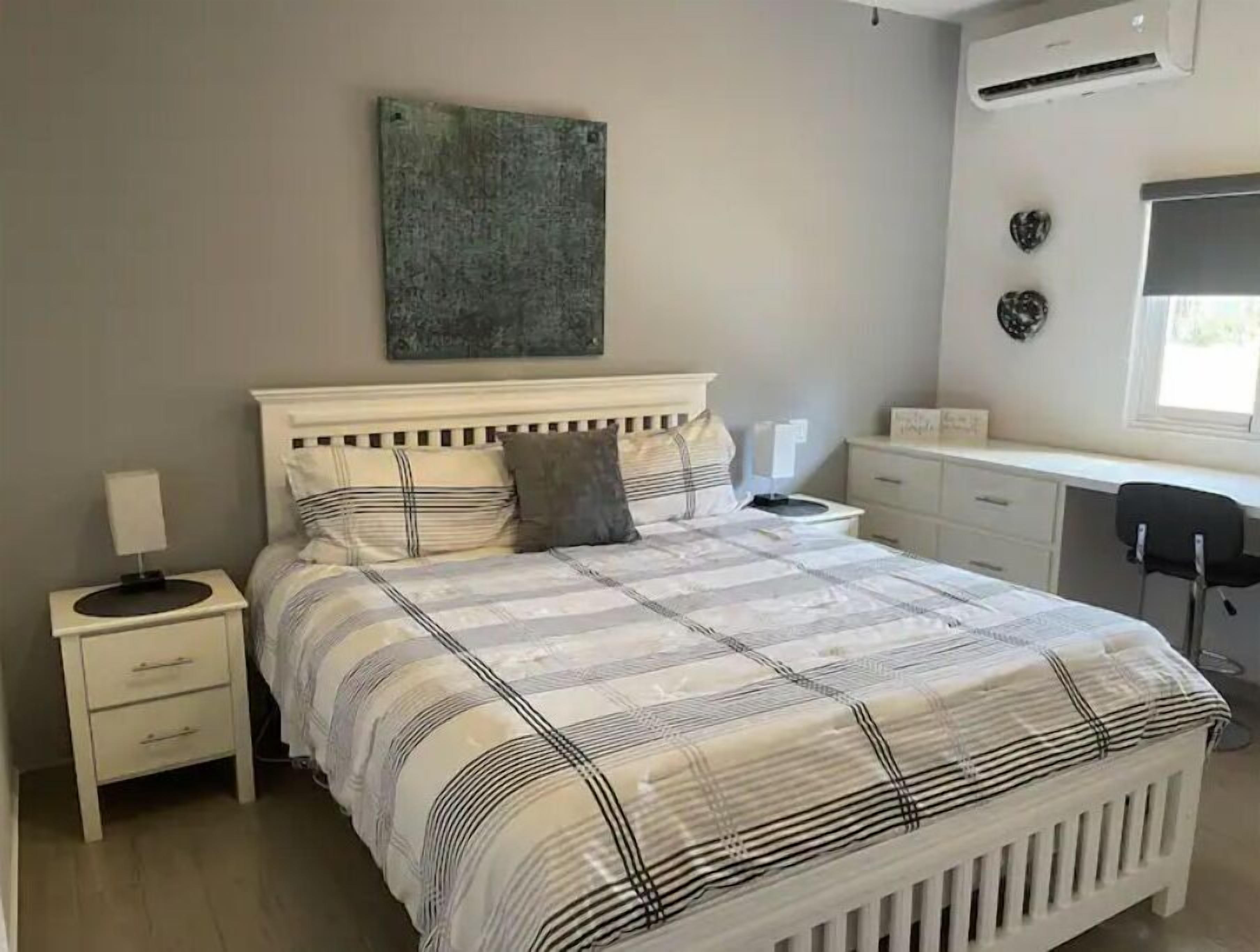 A bedroom with a bed, bedside tables, a desk, and an air conditioning unit.