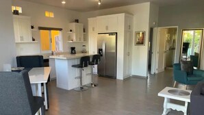 A modern kitchen with white cabinets, a central island with bar stools, a refrigerator, and a dining area with a table and chairs. - 1A Casa Un Amor, Cerritos Beach Condo (El Pescadero)
