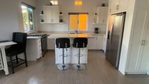 A modern kitchen with white cabinets, a stainless steel refrigerator, a gas stove, and two bar stools. - 1A Casa Un Amor, Cerritos Beach Condo (El Pescadero)