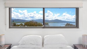 A bedroom with a large window offering a scenic view of mountains and a lake.