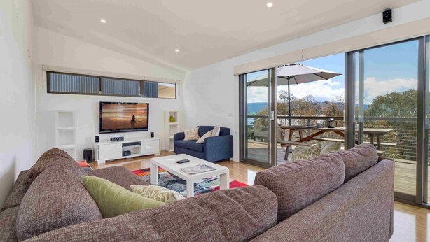 A spacious living room with a large flat-screen TV, a blue sofa, and a large window offering a view of the outdoors.