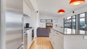 A modern kitchen with a built-in oven, a dining area with a grey sofa, and a large window offering a view of the outdoors.