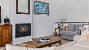 A living room with a fireplace, a sofa, a coffee table, and a painting on the wall. - Stockyards 1 with uninterrupted mountain and lake views (Jindabyne)