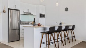 A modern kitchen with a stainless steel refrigerator, a microwave, and a large island with bar stools. - Stockyards 1 with uninterrupted mountain and lake views (Jindabyne)
