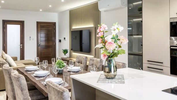 A modern living room with a dining area, a sofa, a TV, and a kitchen with an oven. - Luxurious, spacious fully equipped home in Swieqi (Is-Swieqi)
