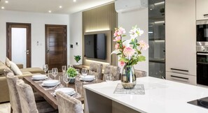 A modern living room with a dining area, a sofa, a TV, and a kitchen with an oven. - Luxurious, spacious fully equipped home in Swieqi (Is-Swieqi)