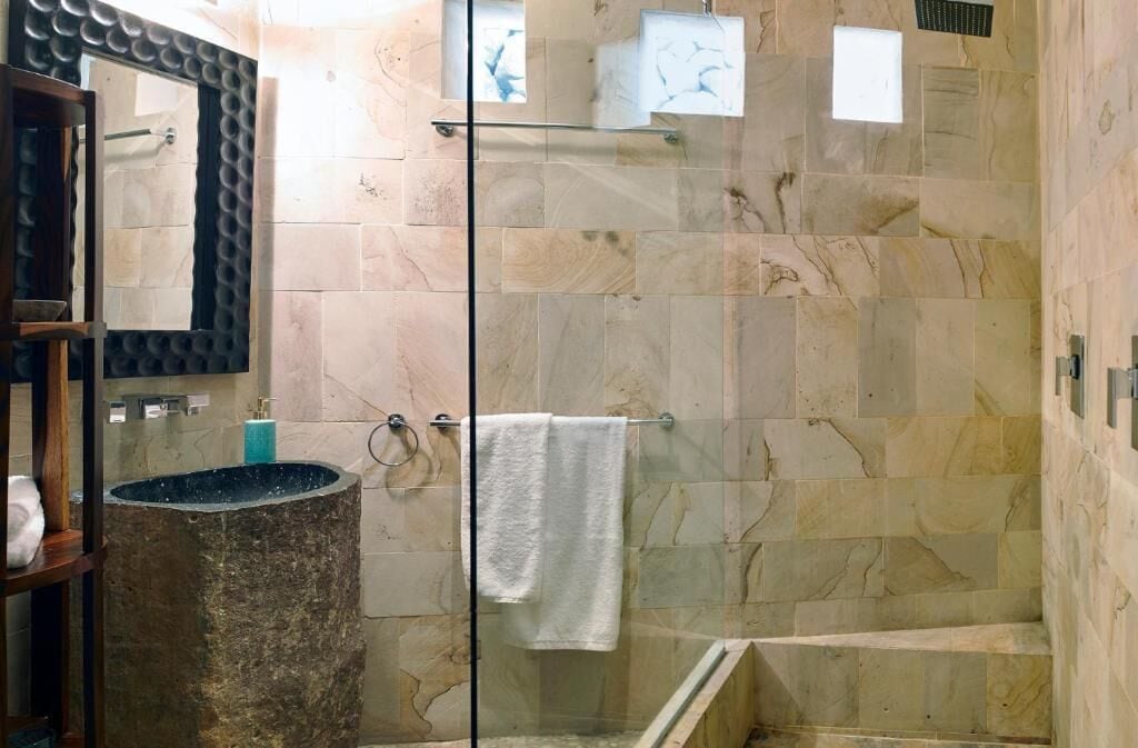 Un baño moderno con cabina de ducha de vidrio, baldosas de mármol, lavamanos empotrado y un perchero para toallas.