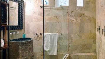 Un baño moderno con cabina de ducha de vidrio, baldosas de mármol, lavamanos empotrado y un perchero para toallas.
