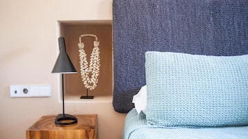 Quarto bem arrumado com mesa de cabeceira de madeira, abajur preto, colar de contas decorativo, almofada azul texturizada e cabeceira azul escura.