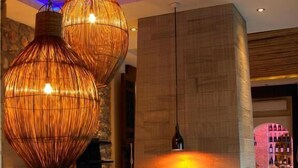 Een gezellige woonkamer met een open haard, een bank, een houten tafel en twee hangende rieten lampen.