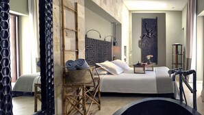 Een moderne hotelkamer met een groot bed, een klein nachtkastje, een geweven stoel en een grote spiegel.