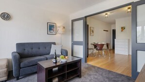 A modern living room with a grey sofa, a wooden coffee table, and a dining area with a table and chairs.