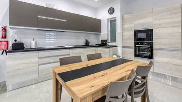 Een moderne keuken met een houten eettafel en stoelen, een inbouwoven en een brandblusser.