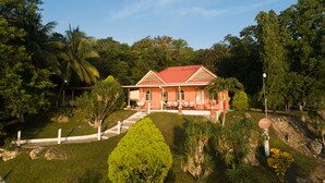 A house with a red roof, surrounded by lush greenery and palm trees.