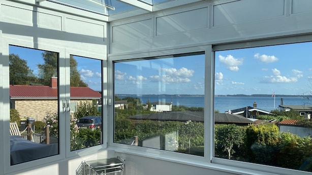 Una veranda con ampie finestre che si affaccia su una zona costiera, un tavolino e una zona relax con cuscini.