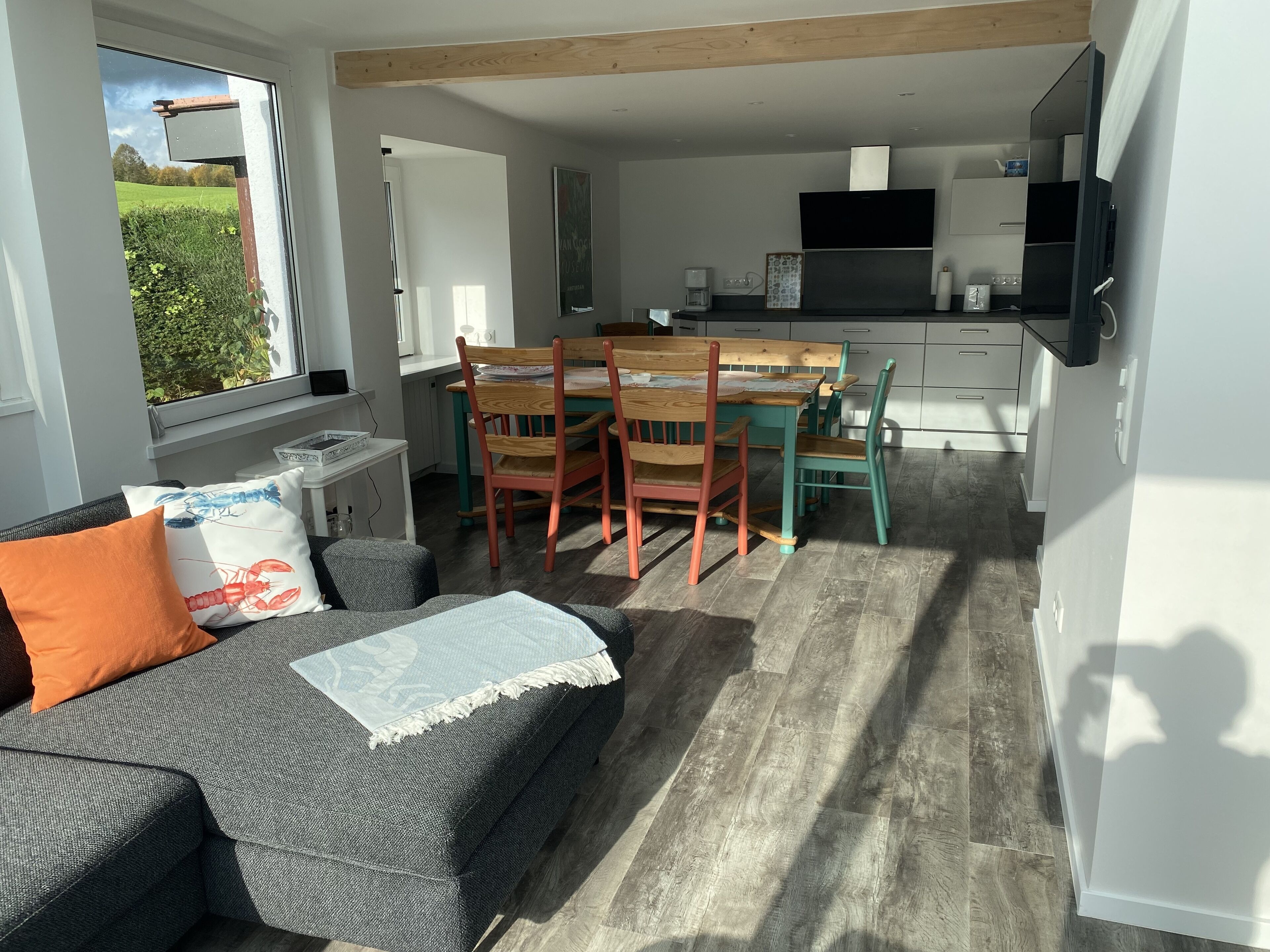 Un espacio de estar acogedor con sofá, una mesa de comedor y sillas, una cocina con televisor, y vistas a zonas verdes.