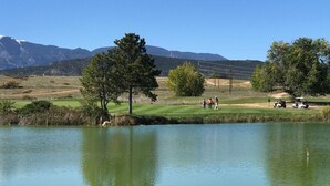 A golf course with a pond, trees, and mountains in the background.