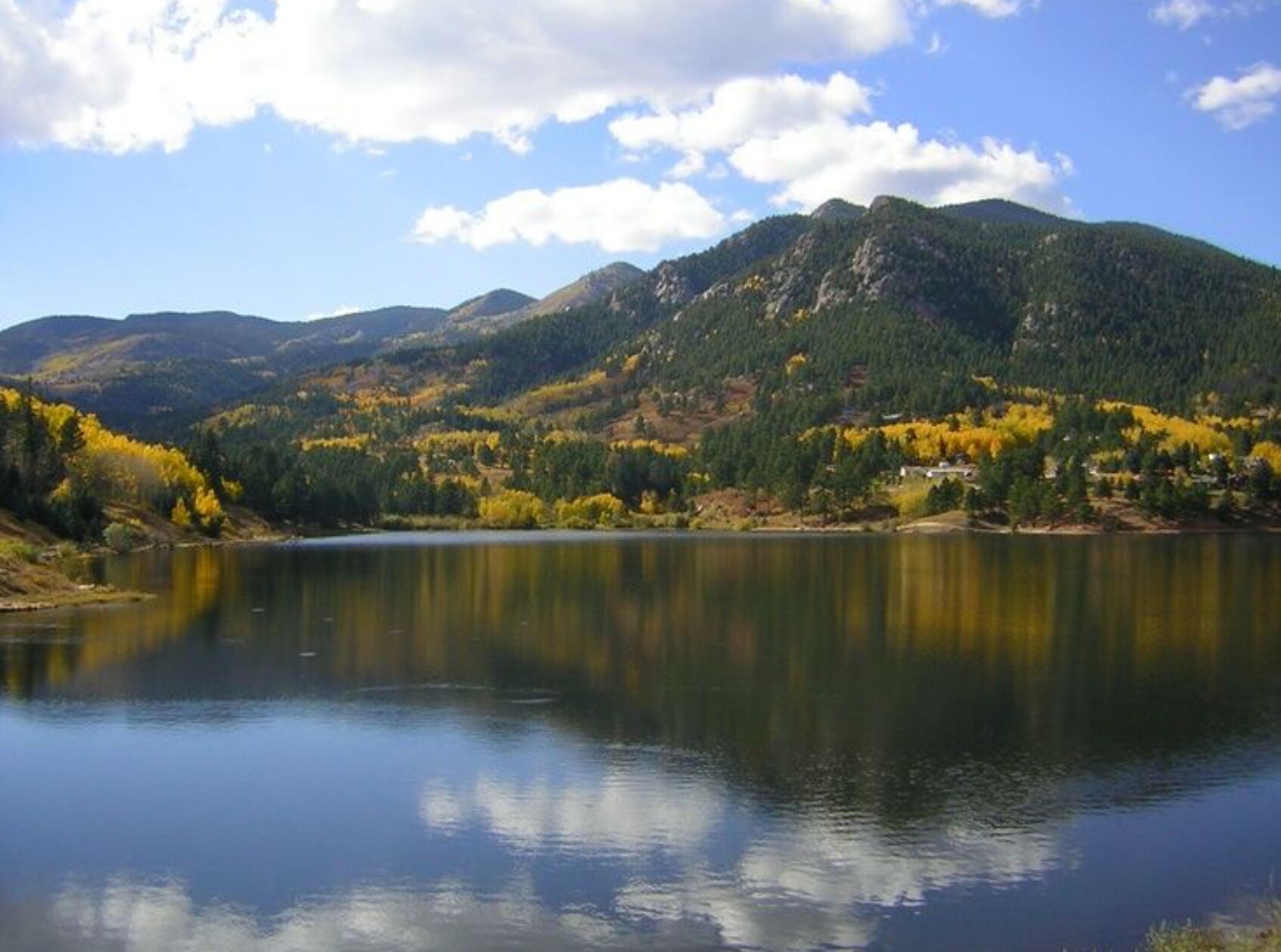 A serene lake surrounded by mountains with autumn foliage, reflecting the sky and trees.