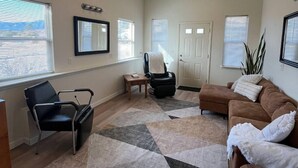 A spacious living room with a large window, a black chair, a brown sofa, and a patterned rug.