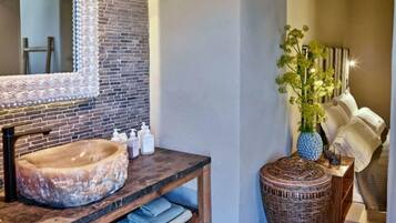 A bathroom with a round sink, a mirror with a brick backsplash, and a wicker basket.