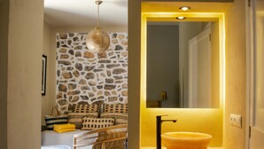 A bathroom with a stone-patterned wall, a wicker chair, a small round table, and a yellow-lit sink. - Gare du Nord Hotel (Sant Joan de Labritja)