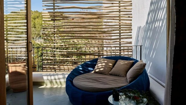 A balcony with a wooden pergola, a blue bean bag chair, and a small round table with a plant and a mug. - Gare du Nord Hotel (Sant Joan de Labritja)