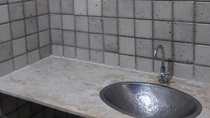 A bathroom with a tiled wall, a round mirror, and a sink. - Ap Banho de Mar (Ondina Salvador)