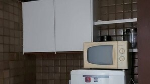 A compact kitchen with a microwave, refrigerator, and a small oven. - Ap Banho de Mar (Ondina Salvador)