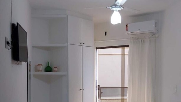 A small, clean room with a bed, a wardrobe, a ceiling fan, and a TV. - Ap Banho de Mar (Ondina Salvador)