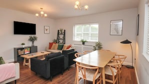 A modern living room with a sofa, dining table, chairs, a TV, and a window with blinds. - The Pheasantry (Bridlington)