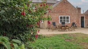 A brick house with a patio, a table with chairs, and a garden with red flowers. - The Pheasantry (Bridlington)
