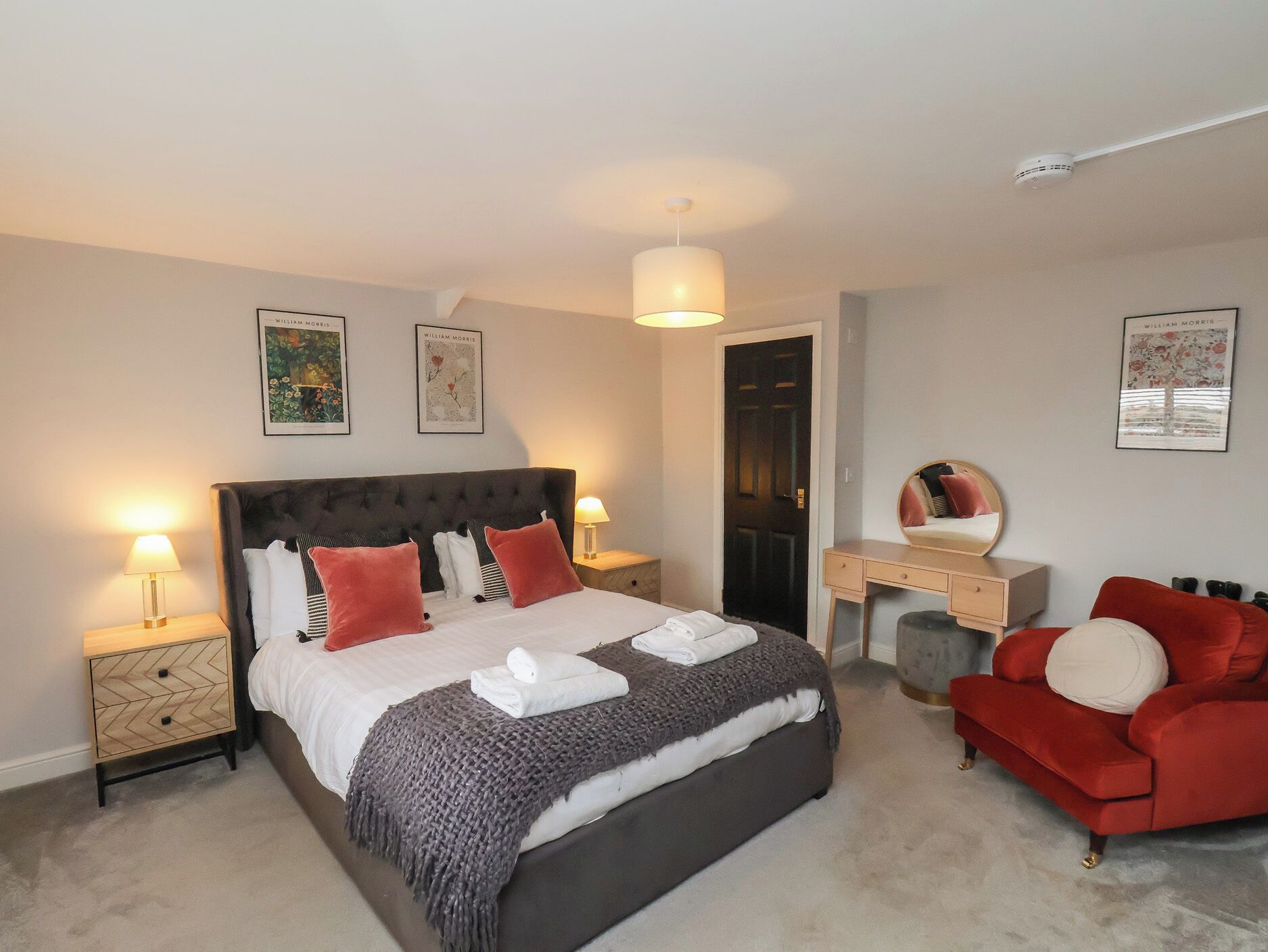 A bedroom with a large bed, bedside tables, a dresser, a mirror, and a red armchair.