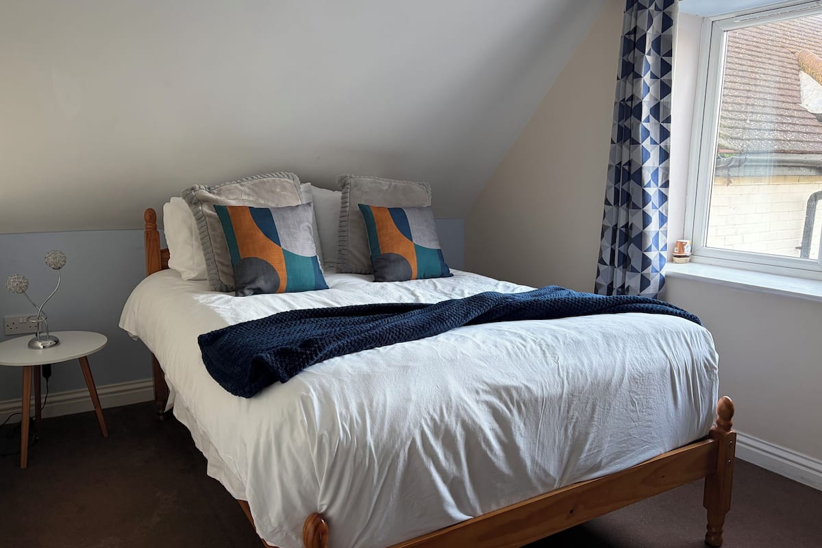 A bedroom with a wooden bed, white bedding, a blue blanket, and patterned pillows.