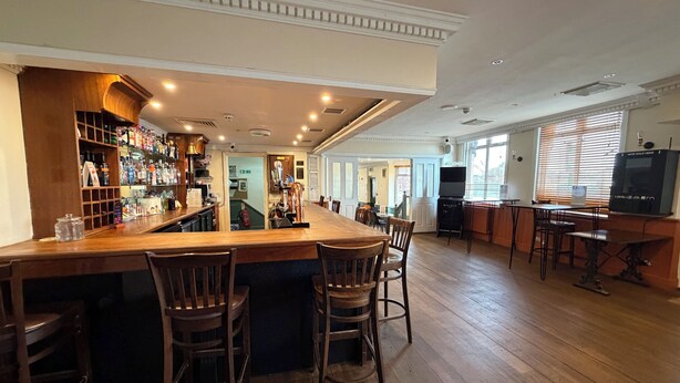 A bar area with wooden bar counter, stools, and shelves stocked with bottles. - Captain Howey Hotel (New Romney)