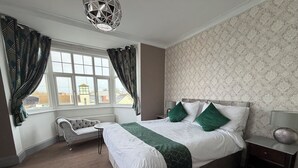 A bedroom with a large bed, a nightstand, a chair, and a window with curtains. - Captain Howey Hotel (New Romney)