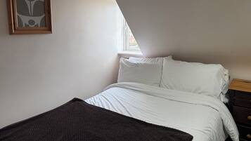 Un dormitorio con cama, ropa de cama blanca, un plaid marrón oscuro, un cabecero de madera, una ventana con vistas y una obra de arte enmarcada en la pared.