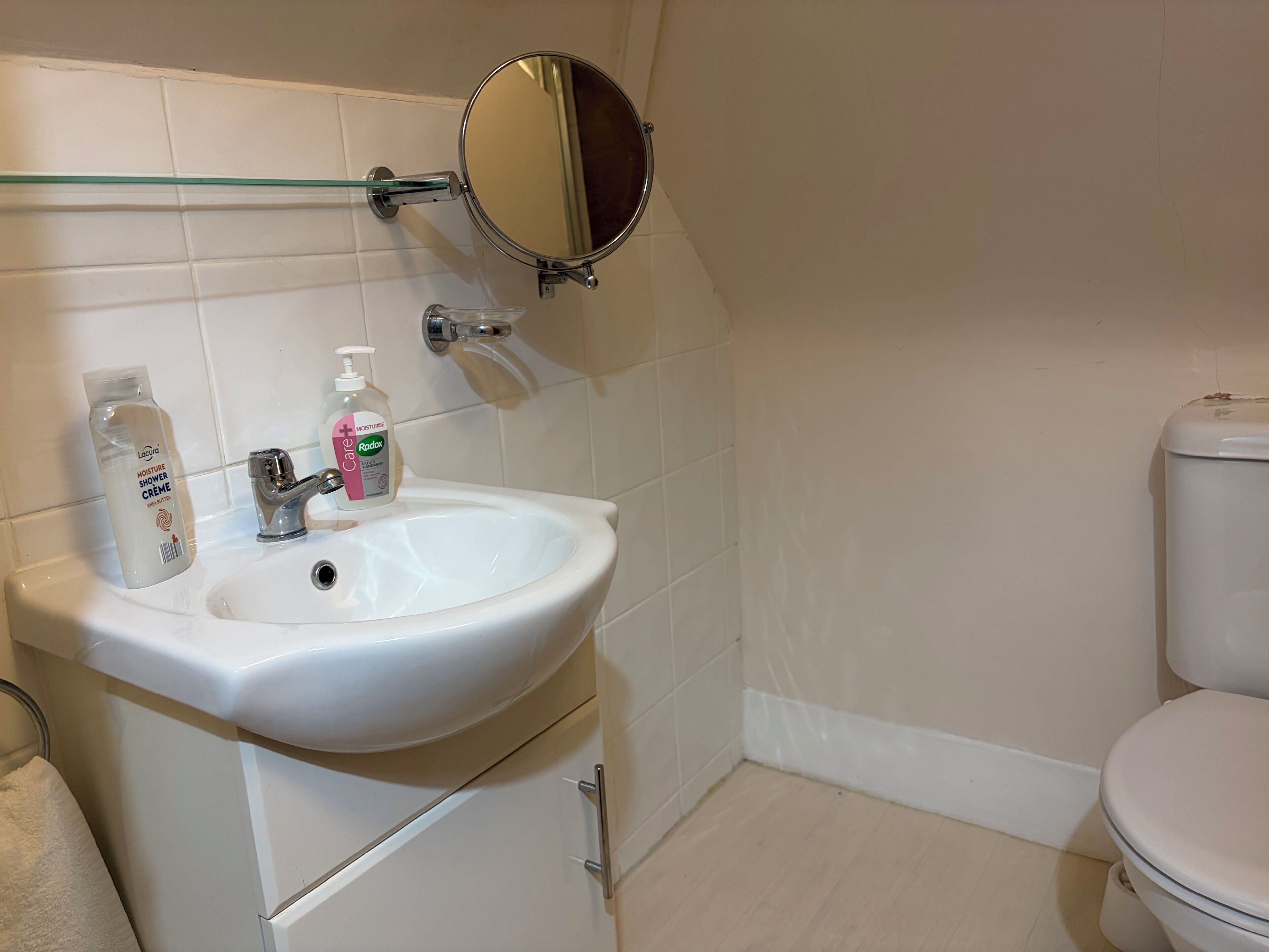 Une salle de bain avec un lavabo blanc, une cabine de douche en verre, un miroir rond et des toilettes.