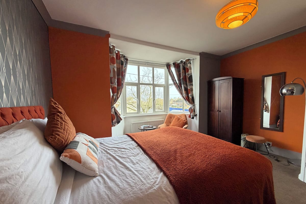 A bedroom with a bed, a chair, a wardrobe, and a window with curtains.