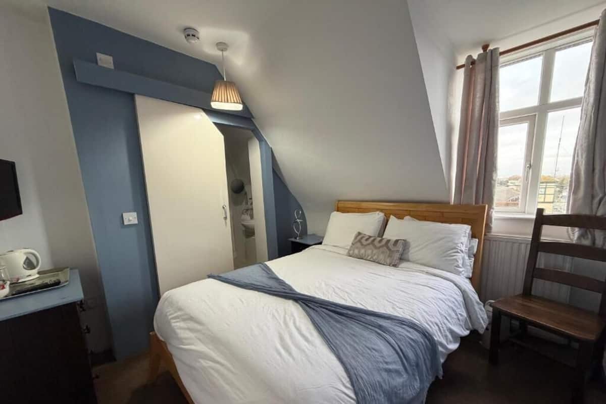 A bedroom with a bed, a desk, a chair, a window with curtains, and a staircase.