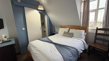 A bedroom with a bed, a desk, a chair, a window with curtains, and a staircase.