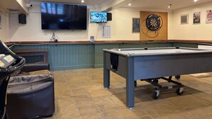 A billiards table, a pool table, and a television screen in a room with a dartboard and a dartboard on the wall. - Captain Howey Hotel (New Romney)